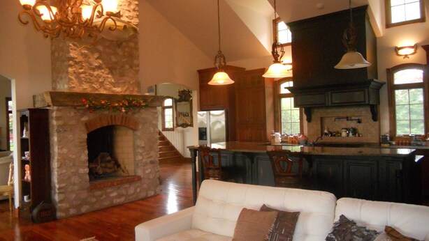 A spacious living area with a stone fireplace, a white sofa, and a kitchen with wooden cabinets and a large island.