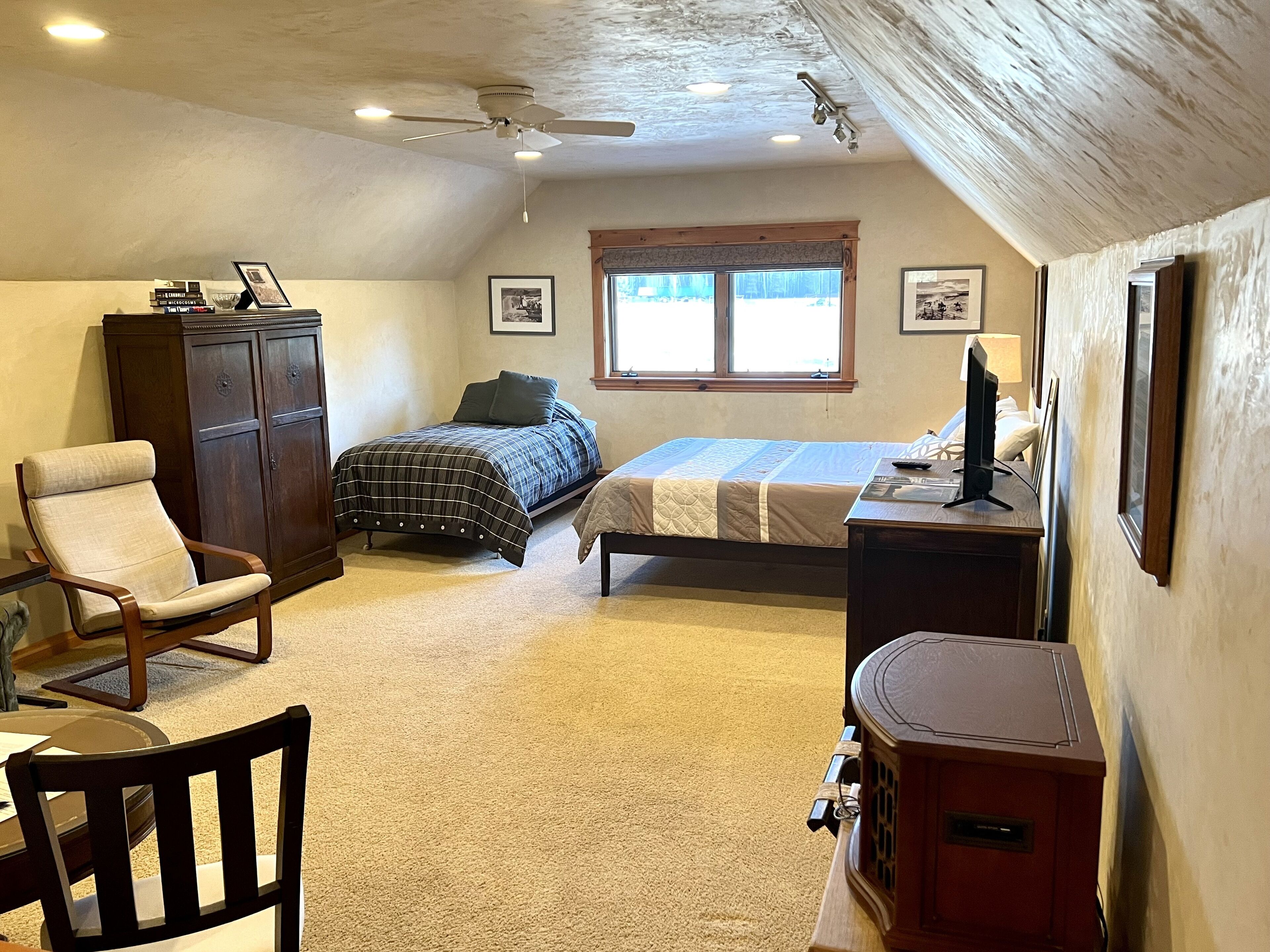 Une chambre avec deux lits, un bureau, une chaise, une armoire et un ventilateur de plafond.