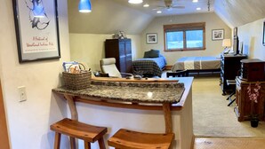 A kitchen with a granite countertop, two wooden stools, a ceiling fan, and a framed artwork on the wall. - Mountain View Studio (Bigfork)