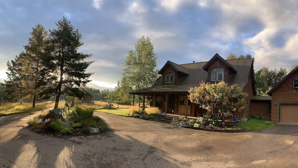 A two-story wooden house with a garage, surrounded by trees and a driveway. - Mountain View Studio (Bigfork)