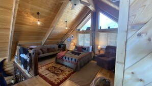 A cozy attic bedroom with a wooden ceiling, a bed with a patterned bedspread, a sofa, and a chair. - Mountainside Luxurious/Rustic Log Home~Majestic Views~Prime Location (Livingston)