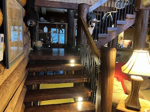 A wooden staircase with a metal railing, a lamp on the landing, and a wall with various items including a skull and antlers.