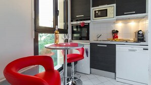 Una cocina moderna con comedor, que incluye una silla roja, una mesita redonda y un ventanal que proporciona luz natural.
