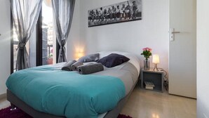 Un dormitorio moderno con cama, cortinas, una mesita de noche con lámpara y un cuadro en la pared.