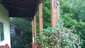 A wooden deck with a covered porch, a hanging planter with flowers, and a view of a green garden. - Spacious house, easy access from Seatac, Seattle & Bellevue.   (Newcastle)