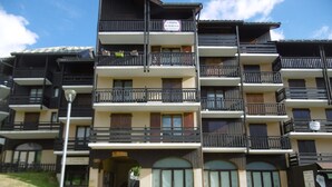A multi-story residential building with balconies, a central entrance, and a clear sky.