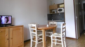 A compact kitchen with a dining table and chairs, a television, and a refrigerator.