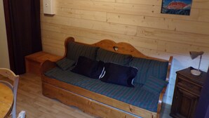 A cozy room with a wooden floor, a wooden sofa with cushions, a small wooden table, and a painting on the wall.