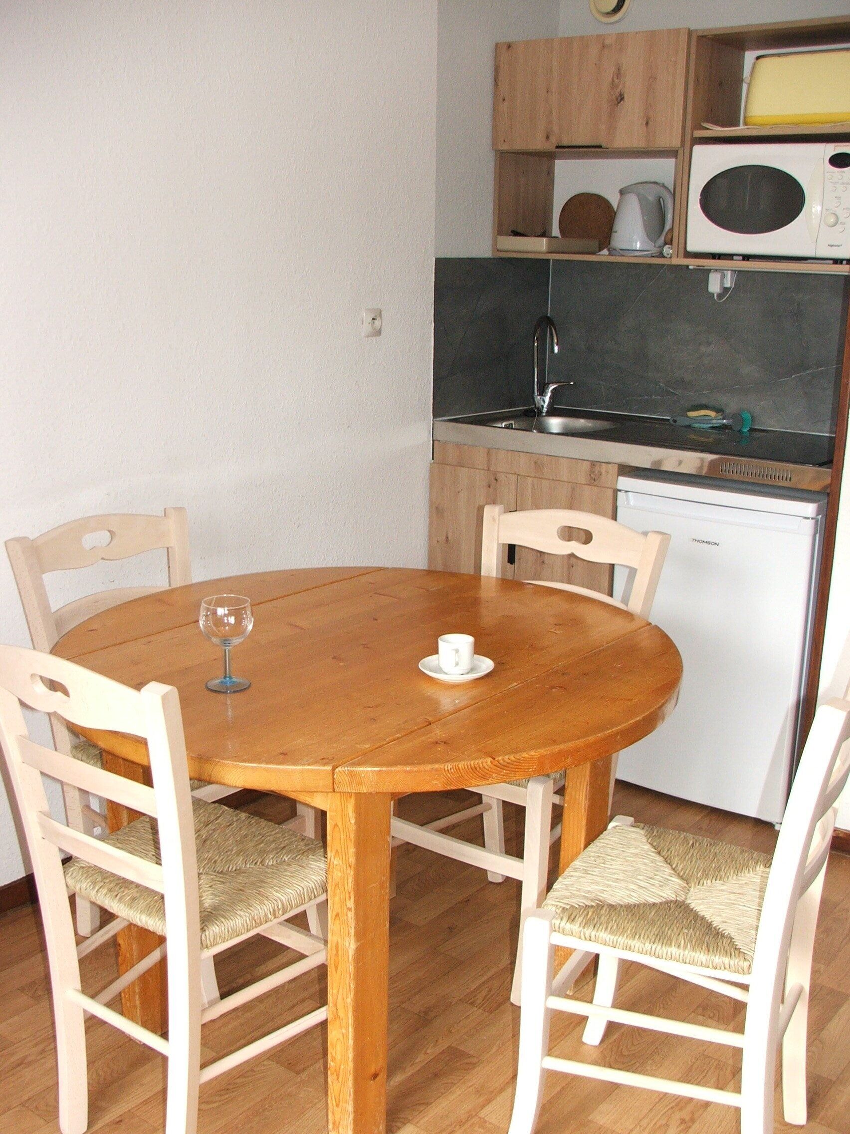 Une petite cuisine équipée d’une table et de chaises en bois, d’un four à micro-ondes, d’une bouilloire et d’un lave-vaisselle.
