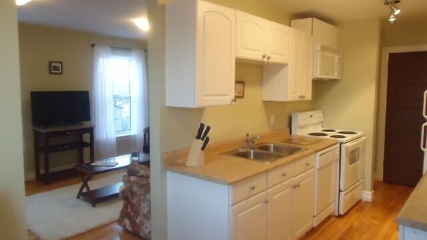 A compact kitchen with white cabinets, a double sink, and a stove. - Great center of historic districts on Water Street (Charlottetown)