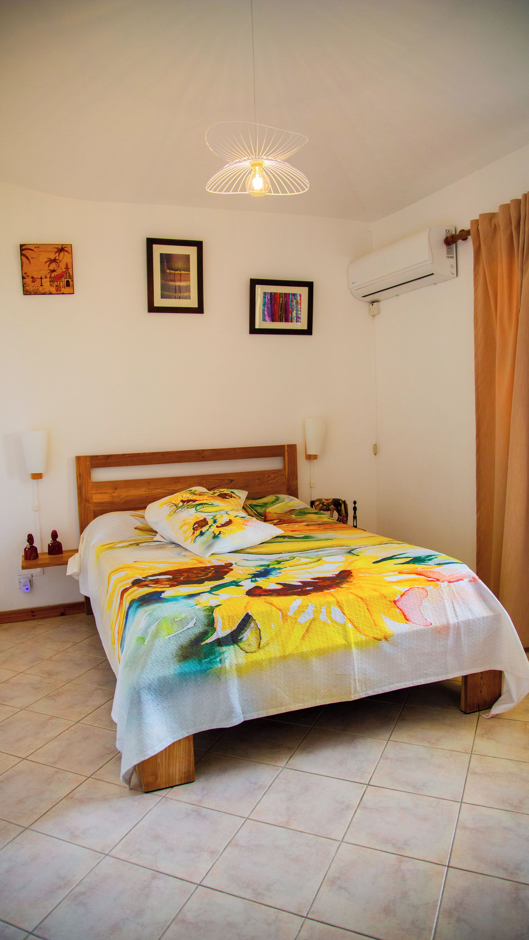 A neatly arranged bedroom with a bed, a bedside table, a wall-mounted air conditioner, and framed artwork on the wall.