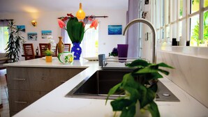 Una cocina moderna con encimera blanca, pileta de acero inoxidable y diversos utensilios de cocina.