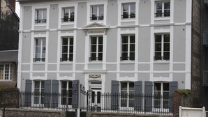 Ein großes, mehrgeschossiges Gebäude mit einer symmetrischen Fassade, das gleichmäßig verteilte Fenster und einen zentralen Eingang mit einem dekorativen Giebel aufweist.