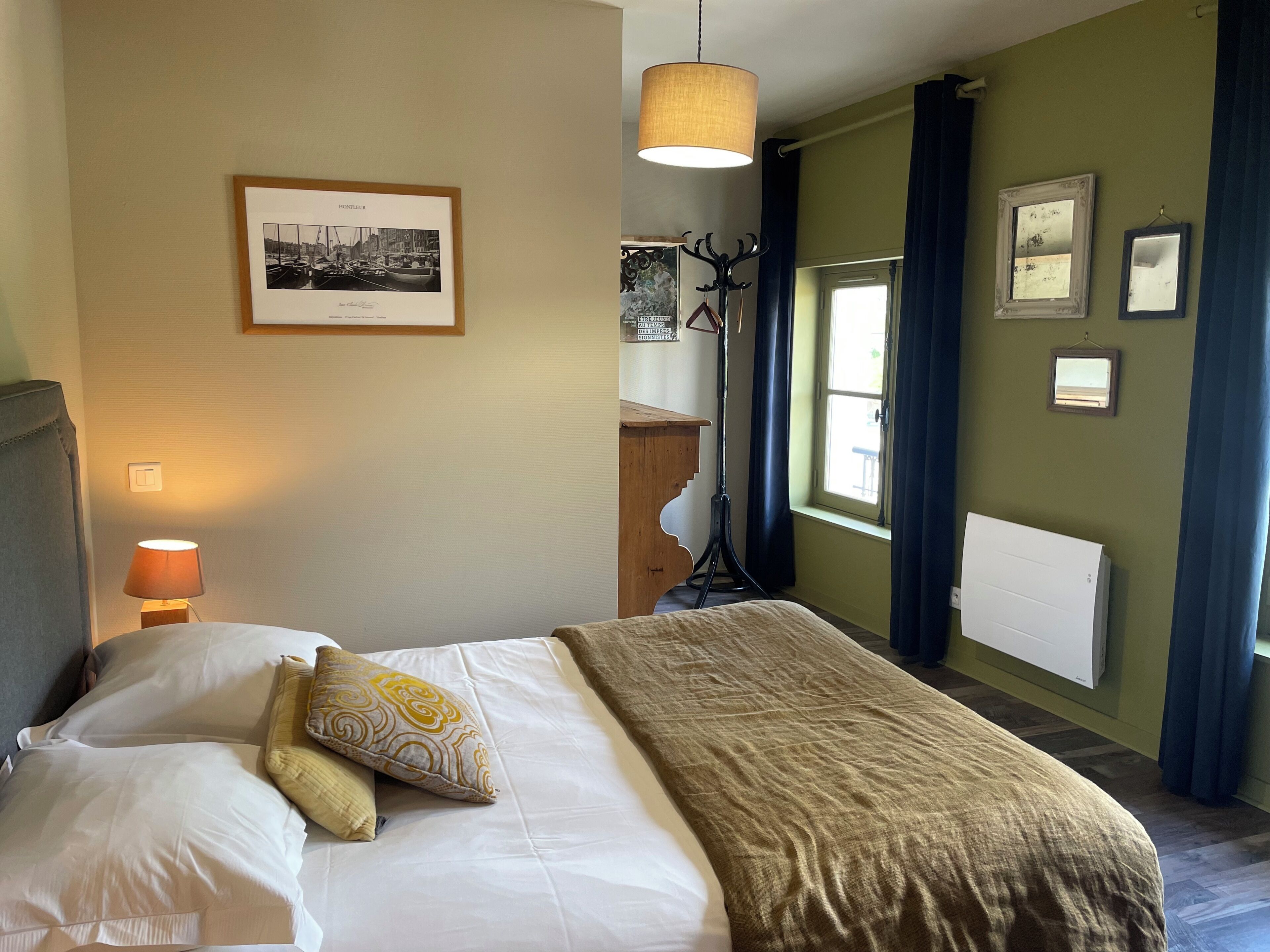 A hotel room with a bed, a framed photograph on the wall, a standing lamp, and a window with curtains.