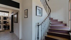 Eine Treppe mit Holzbalken und schwarzen Geländern, die zu einer Empore mit gerahmten Bildern an der Wand führt.