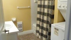 A compact bathroom with a toilet, a sink, a shower with a checkered curtain, and a washing machine.
