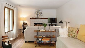 Una sala de estar con un sofá, una mesa de centro con libros, un televisor y una chimenea.