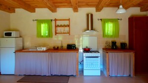 A compact kitchen with wooden beams, a stove, a microwave, and green curtains.