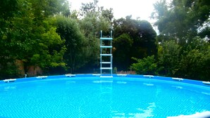 A clear blue swimming pool with a ladder leading into the water, surrounded by lush greenery.