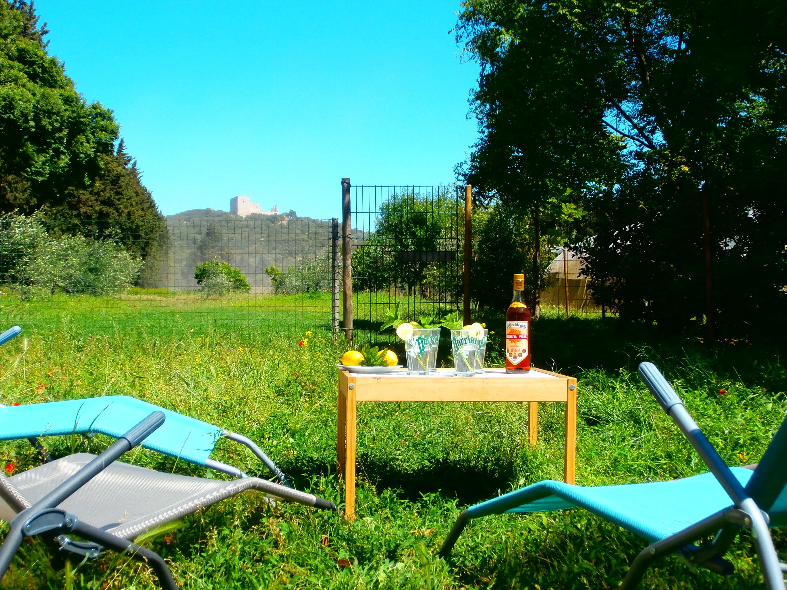Una mesa con una botella y vasos en un espacio al aire libre con césped y sillas.