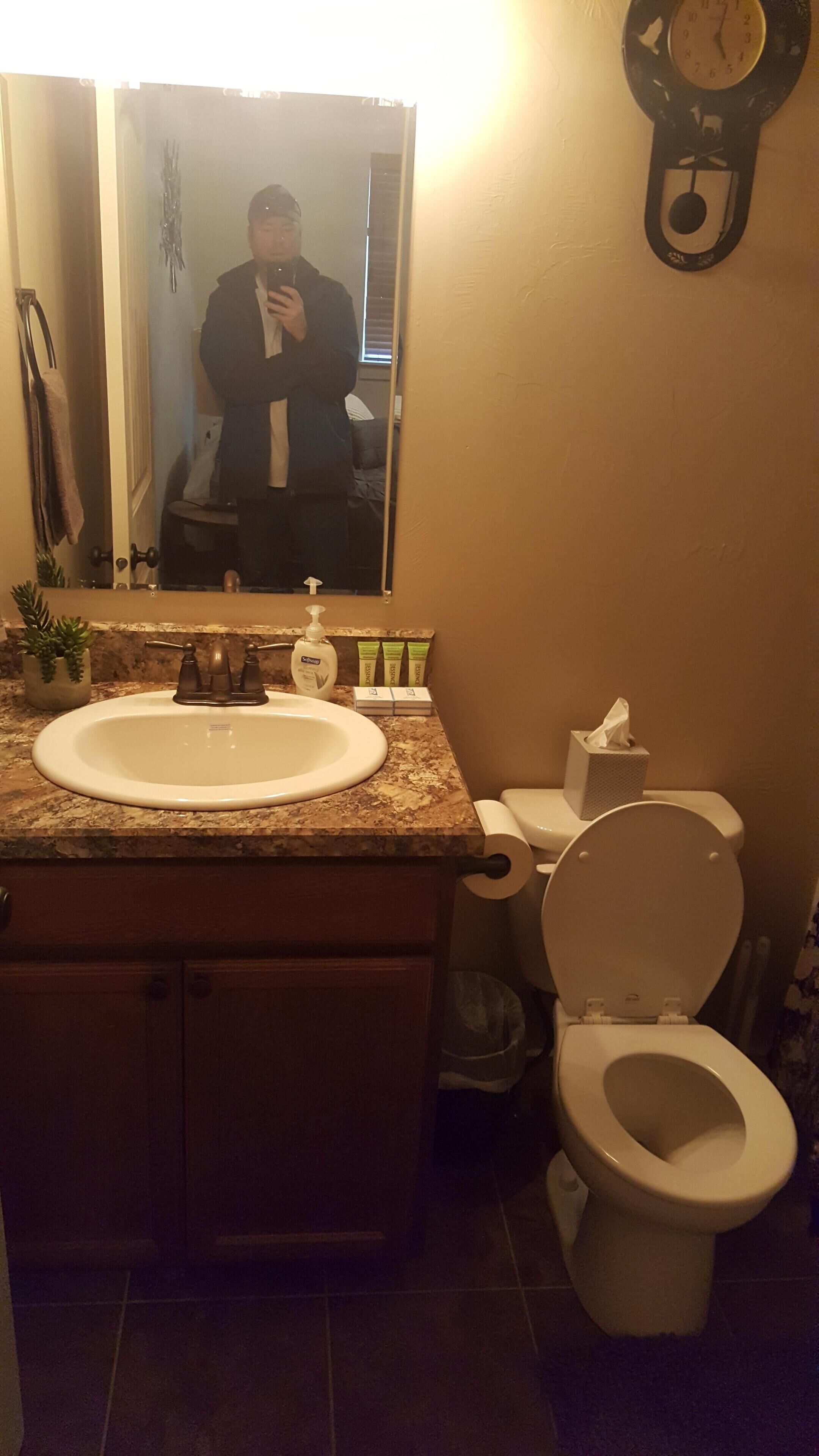 Un bagno con lavandino, specchio, WC e una sveglia appesa al muro.