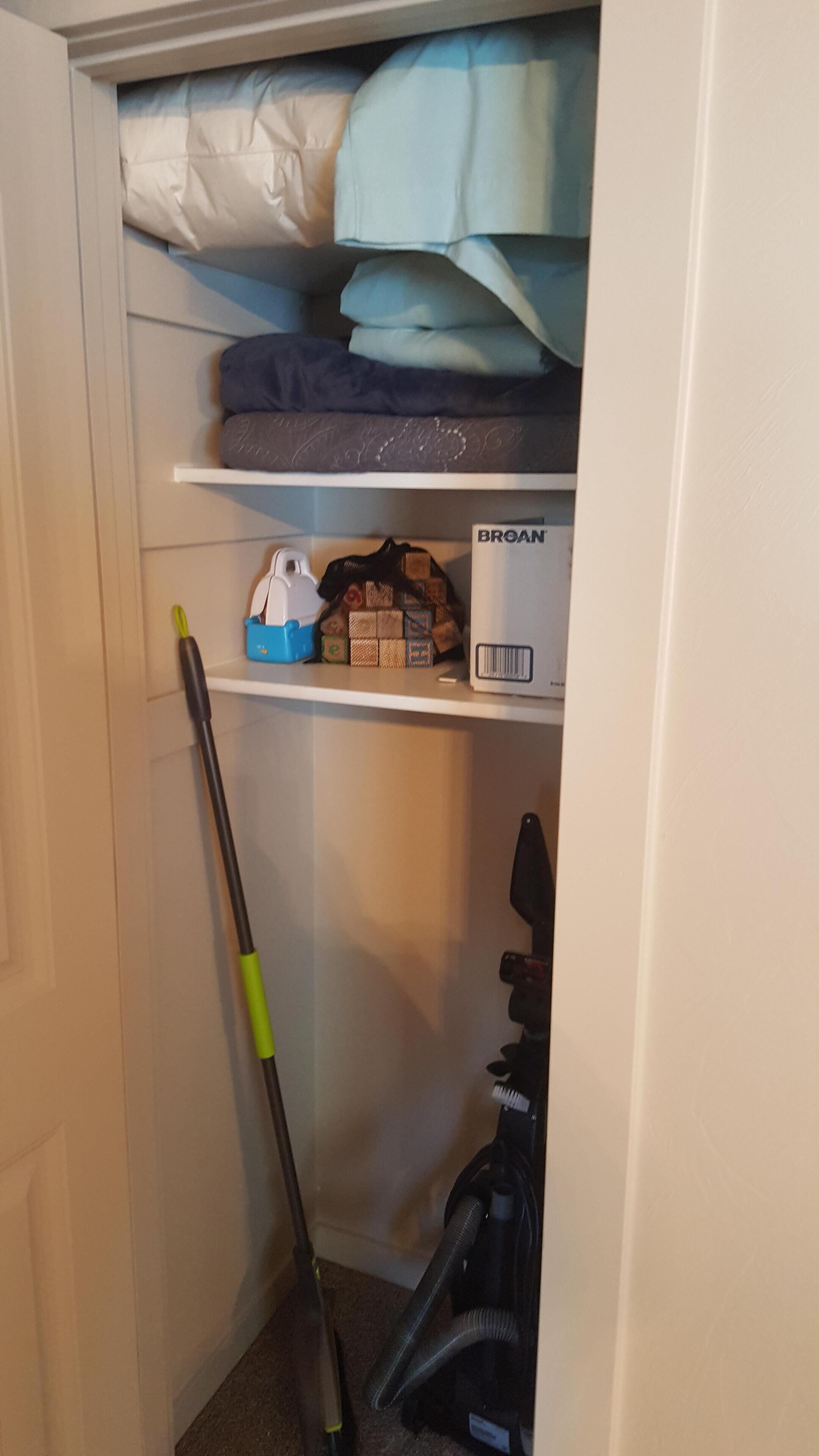 Een kast met opgevouwen kleding, een stofzuiger en een bezem.