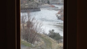 A view through a window of a river flowing through a valley with hills in the background. - Charming Casita With Spectacular River Views  (Riggins)