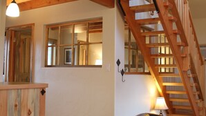 A wooden staircase with a handrail leading to an upper level. A lamp is on the floor next to the stairs. - Charming Casita With Spectacular River Views  (Riggins)