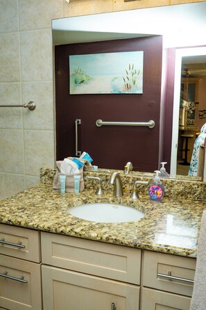 A bathroom with a granite countertop, a sink, a mirror, and a towel rack.