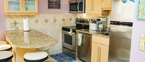 Una cocina con encimera de granito, electrodomésticos de acero inoxidable, armarios de madera y taburetes de bar.