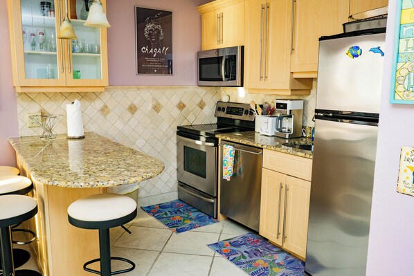 A kitchen with a granite countertop, stainless steel appliances, wooden cabinets, and bar stools.