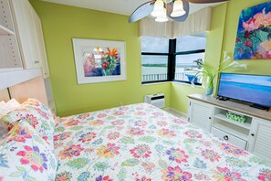 A bedroom with a bed, a television, a window with a view, and a painting on the wall.
