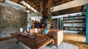 A cozy living room with a stone wall, a wooden table with a candle, a leather sofa, and a wooden floor. - Breakfast With Toucans And Monkeys (San Miguel)