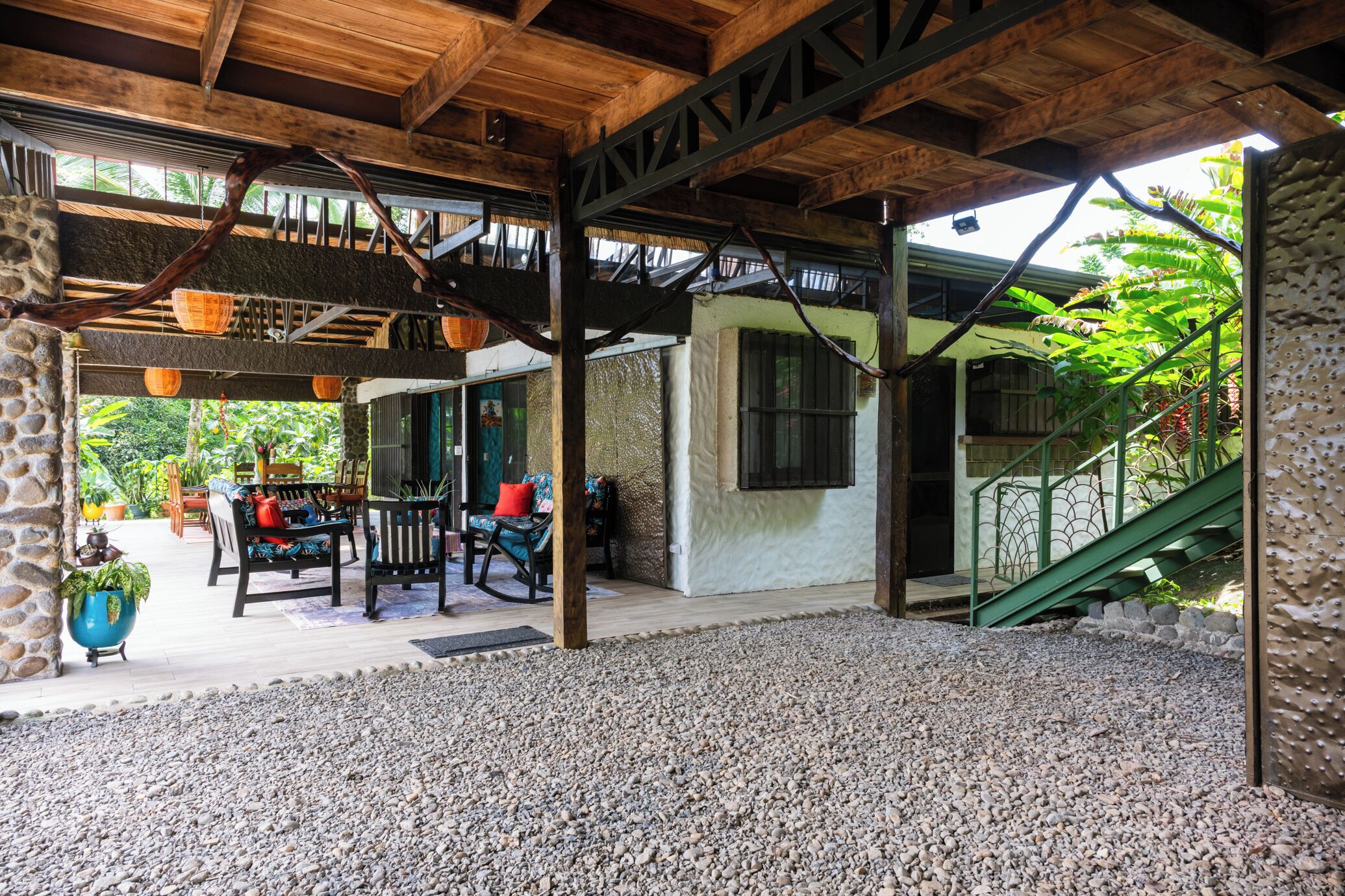 Eine Terrasse im Freien mit Holzboden, Steinwänden und Kiesboden. Es gibt einen Sitzbereich mit Tisch und Stühlen sowie eine Treppe zu einer erhöhten Ebene.