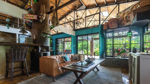 A spacious room with a large window, a wooden table, a leather sofa, and a hanging light fixture. - Breakfast With Toucans And Monkeys (San Miguel)