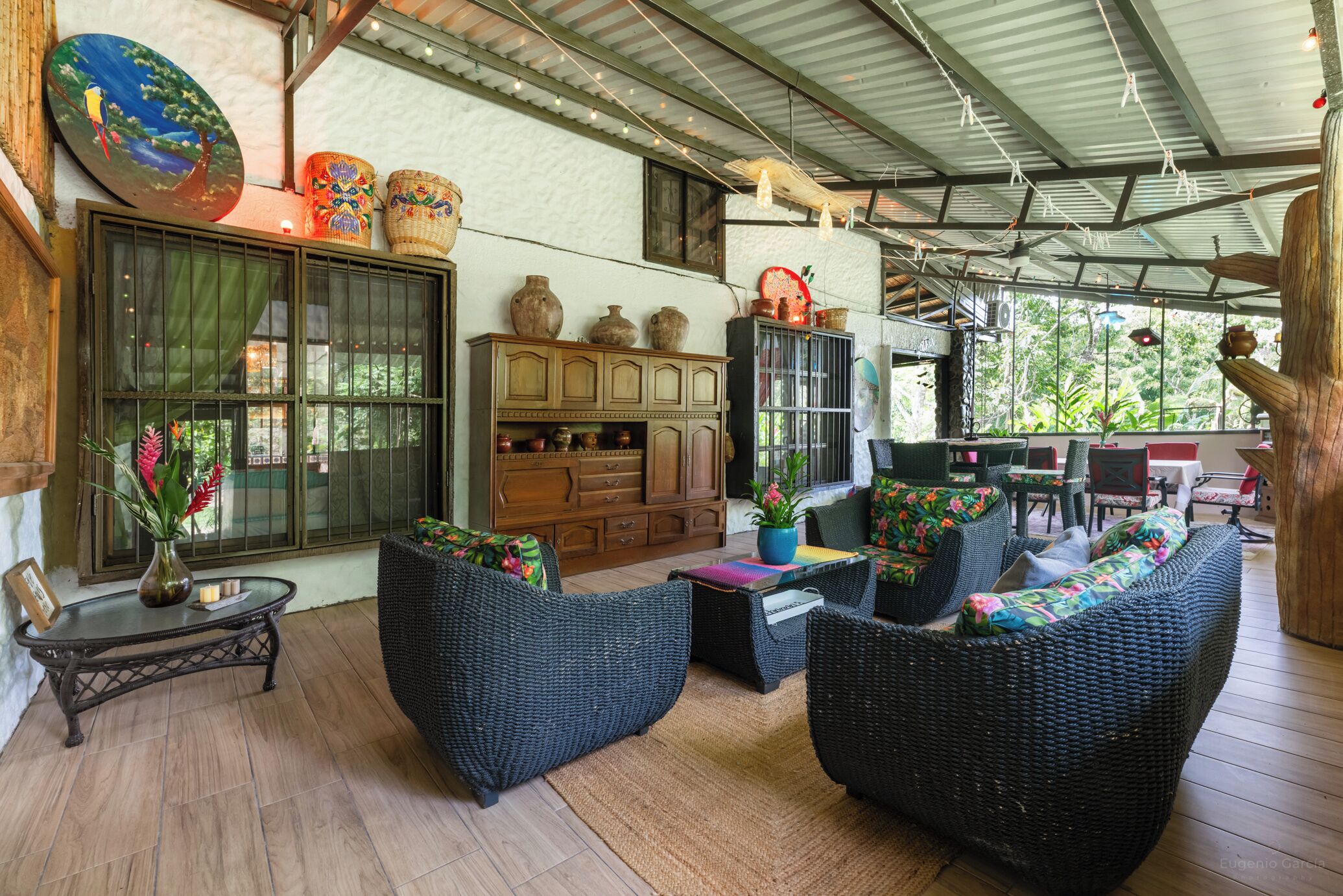 Un espace extérieur abrité, aménagé avec des meubles en osier, un buffet en bois et des objets de poterie décoratifs.