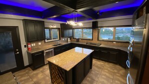 Une cuisine moderne avec des meubles de couleur sombre, des plans de travail en granit, un îlot central et une vue sur un lac grâce à de grandes fenêtres.