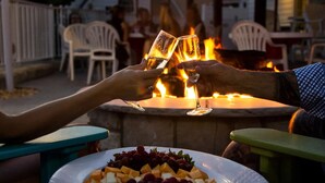 Deux personnes trinquent avec des verres à une table, avec un foyer en arrière-plan.