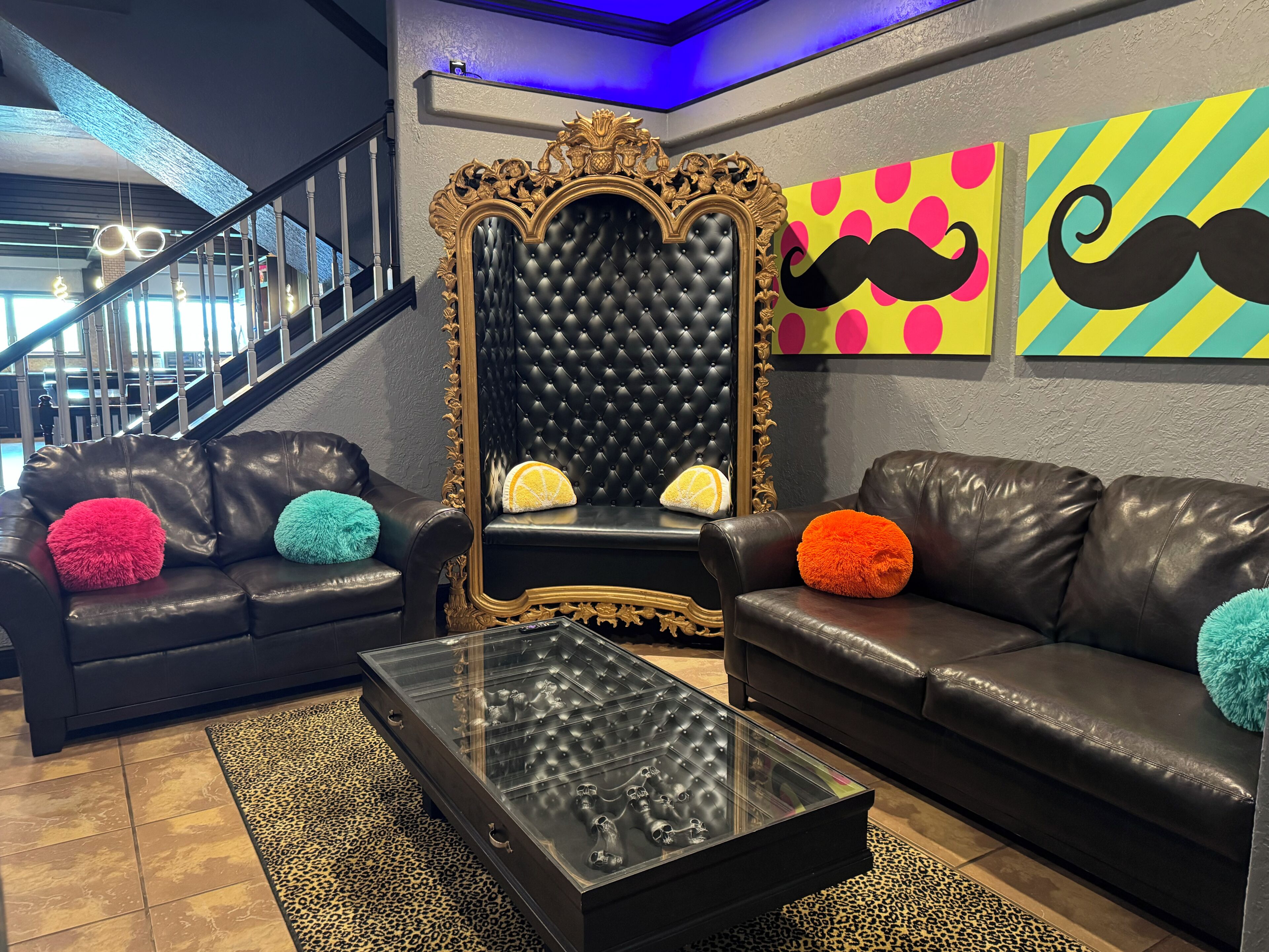 Un salon moderne avec un canapé en cuir noir, une table basse en verre et un miroir décoratif doté d’un cadre orné.