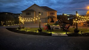 Une maison en pierre avec un garage, un espace extérieur aménagé pour s’asseoir et des guirlandes lumineuses.