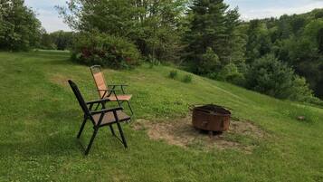Un espace extérieur verdoyant avec un foyer en métal et deux chaises.
