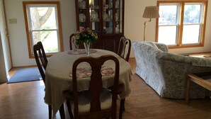 Un coin repas comprenant une table ronde, des chaises, un vase de fleurs, un meuble avec des portes en verre et un canapé.