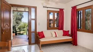 Une pièce avec un canapé en bois, des rideaux rouges et une vue sur un jardin, visible à travers une porte vitrée.