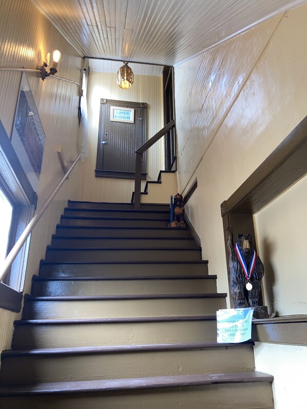 A wooden staircase with a metal handrail, a sign indicating a linen room, and a statue with a medal. - Adults Only, King One Bedroom, Converted 1894 Historic Hotel,Downtown Buffalo Wy (Buffalo)