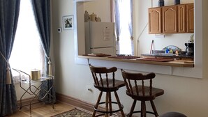 A compact kitchen with a refrigerator, wooden cabinets, and a dining area with two chairs. - King One Bedroom, Converted 1894 Historic Hotel, Downtown Buffalo Wyoming (Buffalo)