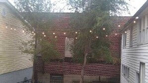 A brick building with a tree in the center, surrounded by a fence and string lights. - Wine Alley West Suite (Hermann)
