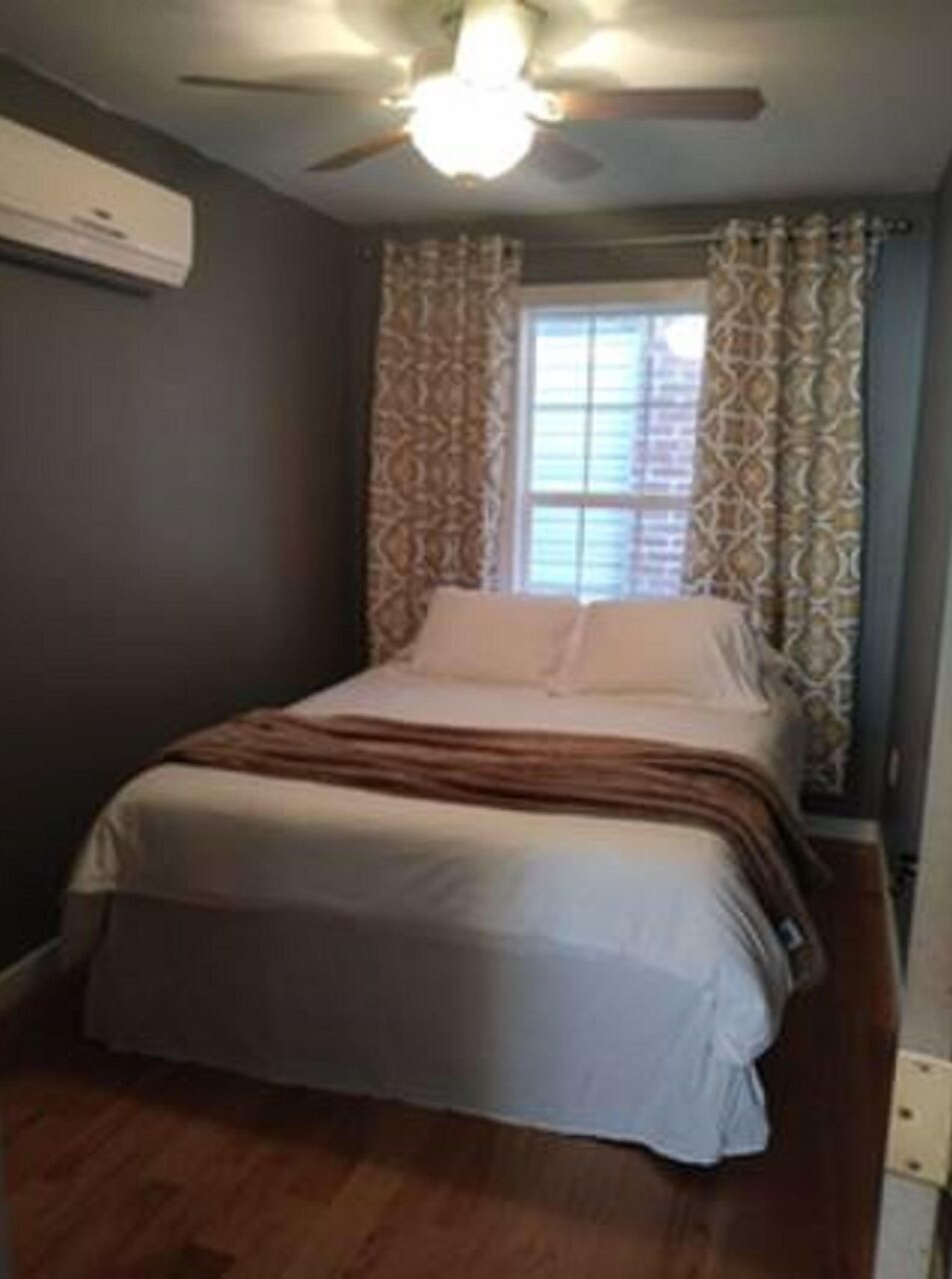 Une chambre à coucher avec un lit, un ventilateur de plafond et une fenêtre ornée de rideaux à motifs.