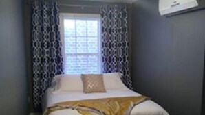 A bedroom with a bed, a ceiling fan, a window with patterned curtains, and a wooden floor. - Wine Alley West Suite (Hermann)