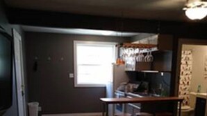 A compact living space with a kitchen area, a dining table with stools, and a television. - Wine Alley West Suite (Hermann)
