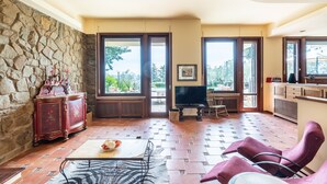A spacious living area with a stone wall, a red antique cabinet, a television, and a view through large glass doors. - Modern Panoramic Villa with swimming pool in Florence - Tuscany (Firenze)
